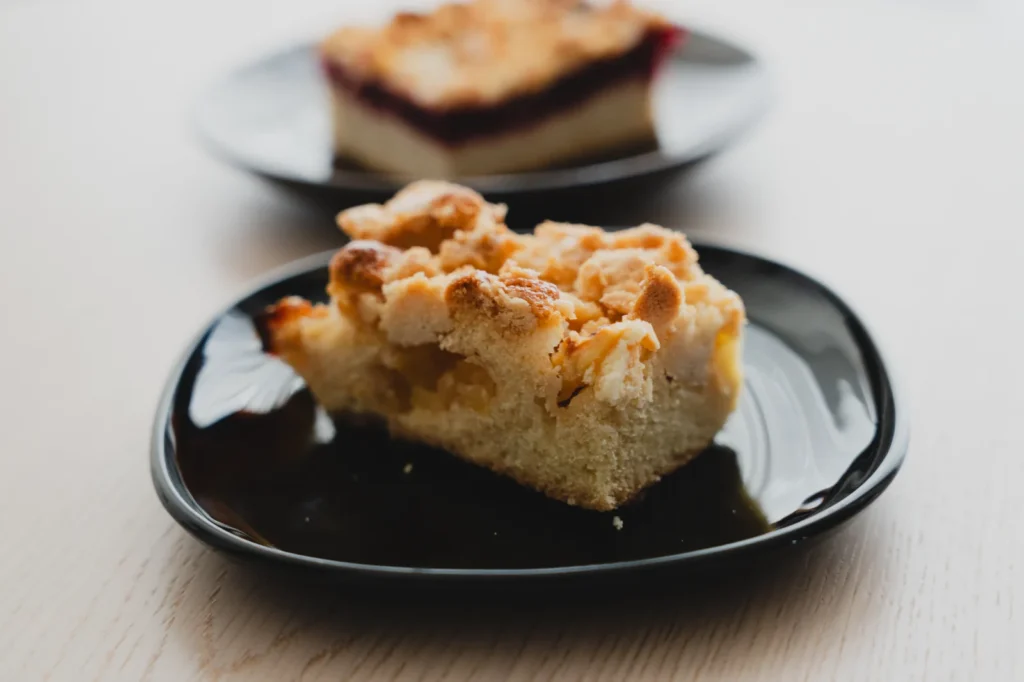 blueberry buckle poke cake with golden streusel topping and syrupy blueberry holes on a white plate