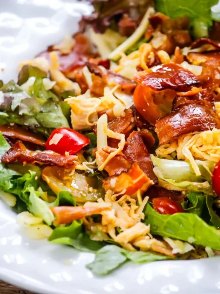 broccoli salad recipe with bacon and cheese showing raw broccoli florets, crispy bacon pieces, and cheddar cubes in creamy dressing on a white plate
