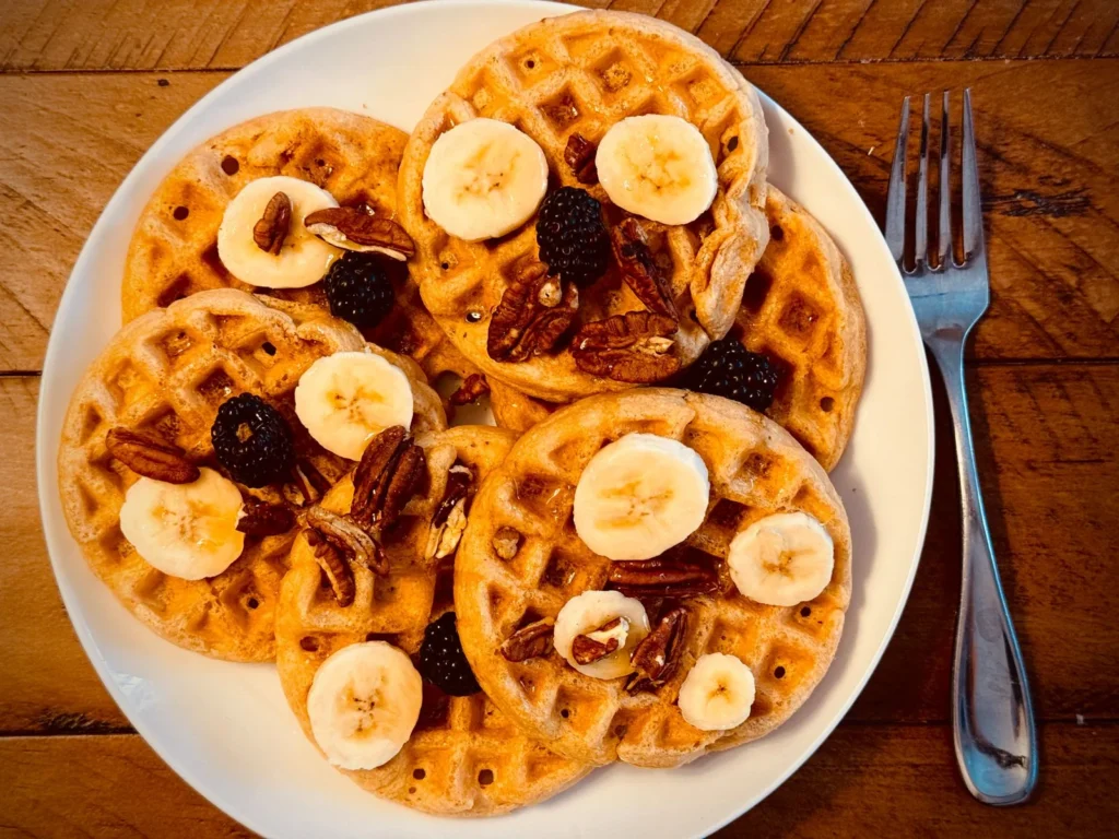 butternut squash waffles recipe with golden crisp waffles topped with maple butter and pecans on a white plate