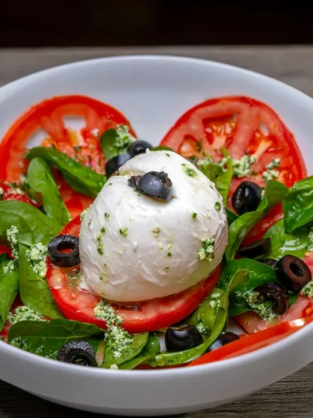 caprese pasta salad with pesto in a white bowl with cherry tomatoes, mozzarella pearls, and basil leaves