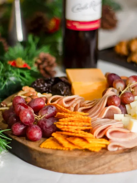 charcuterie board ideas for beginners with cheddar cubes, goat cheese log, prosciutto, salami, grapes, and olives on a wooden board