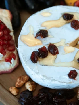 cheese ball recipe for parties showing a round cream cheese ball coated in toasted pecans and dried cranberries on a white platter