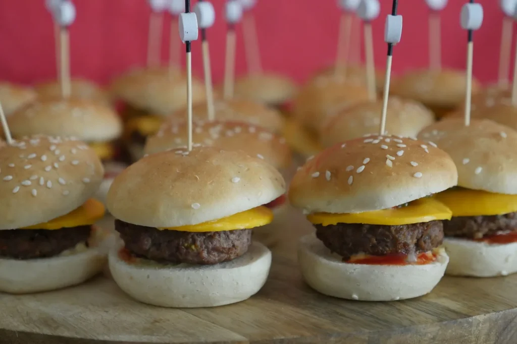 cheeseburger slider with hawaiian roll pulled apart on a tray showing beef, american and cheddar cheese, and sesame top