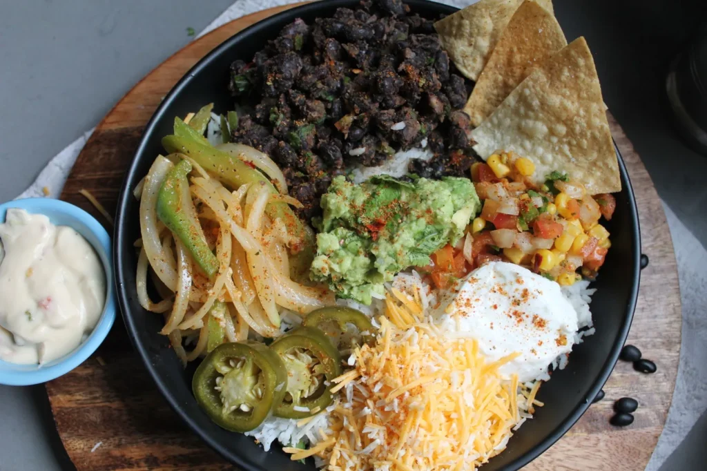 cheesy tex mex sour cream sauce in a white bowl with shredded cheddar, lime wedge, and tortilla chips