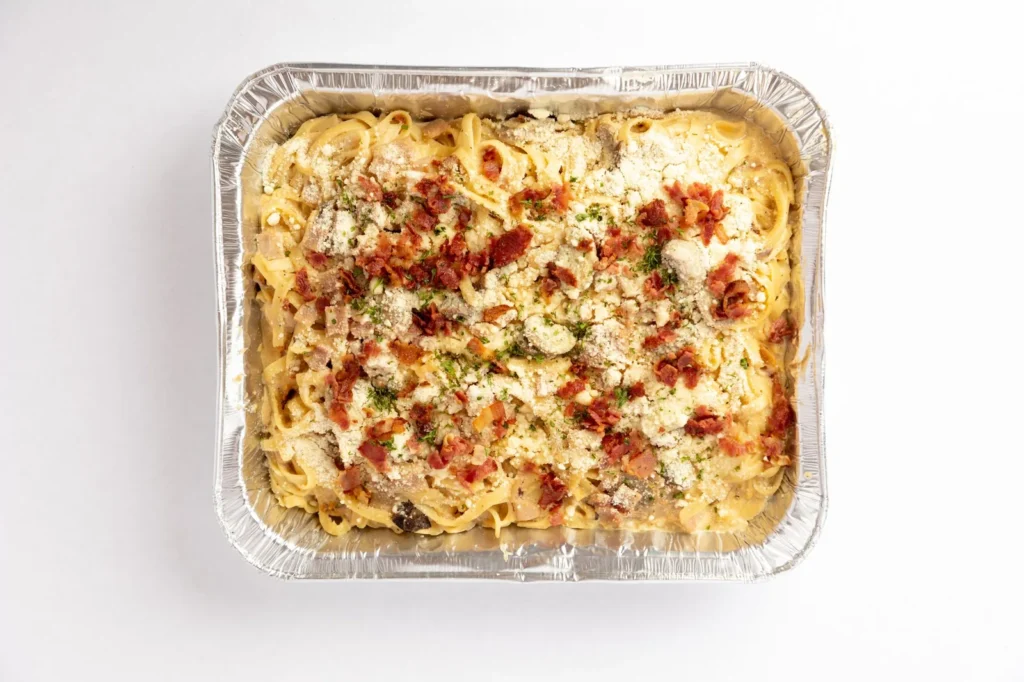 chicken and bacon pasta bake in a white dish with golden cheddar crust, crispy bacon bits, and penne tubes