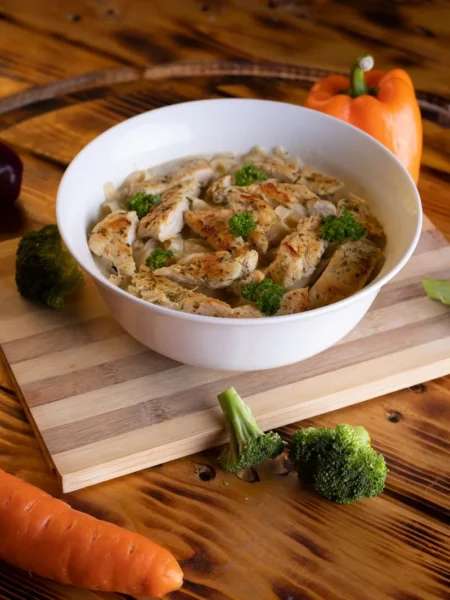 chicken broccoli cheddar soup in a white bowl with tender chicken pieces, green broccoli, and melted sharp cheddar on a wooden table
