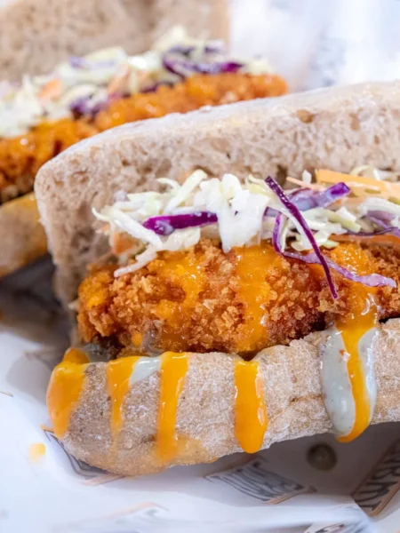 chicken cutlet sandwich recipe with golden fried chicken cutlet, cabbage slaw, and toasted roll on a plate