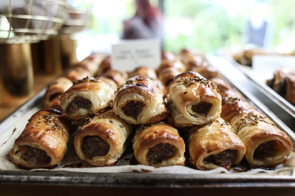 chicken sausage rolls recipe with golden puff pastry, seasoned ground chicken filling, and flaky crisp crust on a tray