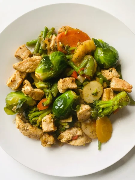 chicken stir fry recipe with vegetables showing seared chicken bites, red and yellow peppers, broccoli, and glossy soy garlic sauce on a white plate