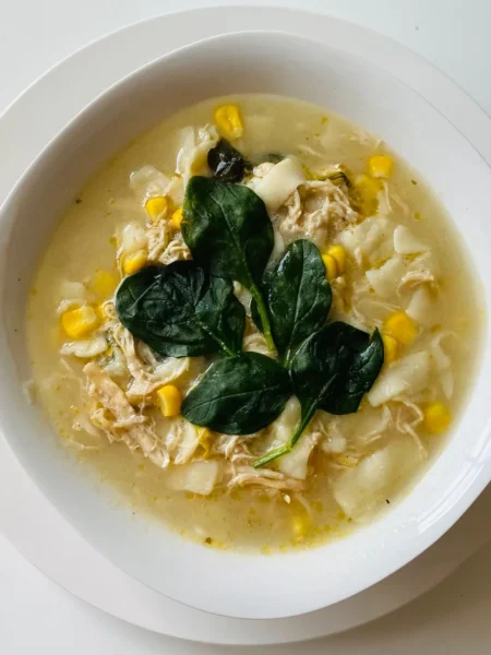 chicken taco soup recipe in a white bowl with shredded chicken, black beans, corn, and cheddar on top