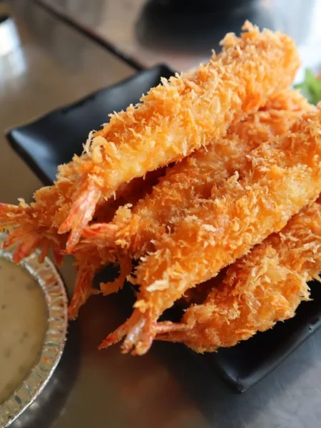 coconut shrimp recipe with golden crisp shredded coconut crust on tender fried shrimp served on a white plate with dipping sauce