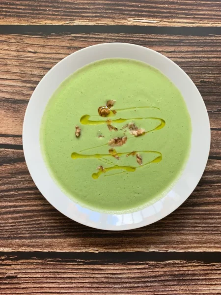 creamy broccoli soup recipe in a white bowl with smooth pale green blended soup and a swirl of cream on top