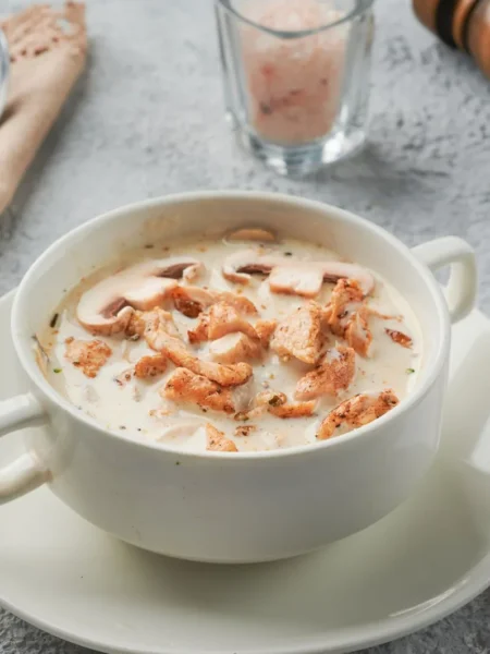 creamy chicken and rice soup in a white bowl with tender chicken pieces, soft rice, and carrot slices in a silky broth