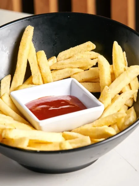 creamy ketchup in a white bowl with a spoon and fries dipped in the smooth red sauce
