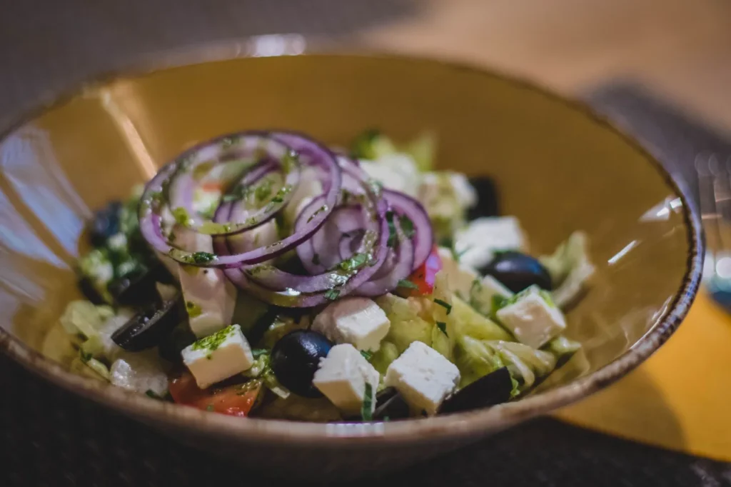 greek cucumber salad with peeled cucumber slices, red onion, tomato wedges, kalamata olives, and crumbled feta in a white bowl