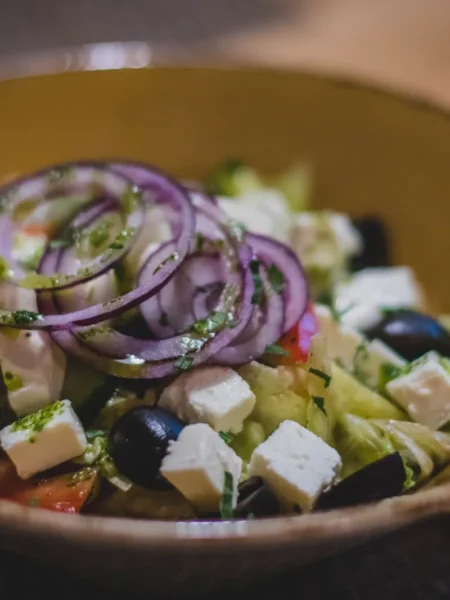 greek cucumber salad with peeled cucumber slices, red onion, tomato wedges, kalamata olives, and crumbled feta in a white bowl