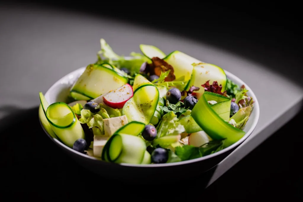 grilled zucchini salad recipe with charred squash planks, lemon dressing, feta, and pine nuts on a white plate