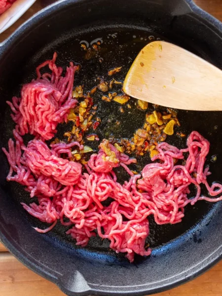 ground beef recipes for tight budgets shown as a skillet of rice lentils and browned beef with cabbage on top