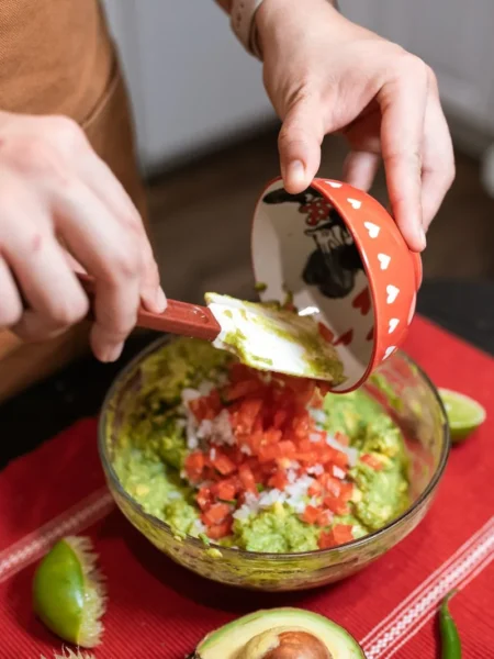 guacamole recipe with fresh lime showing chunky mashed avocado with tomato cilantro and lime wedge in a bowl