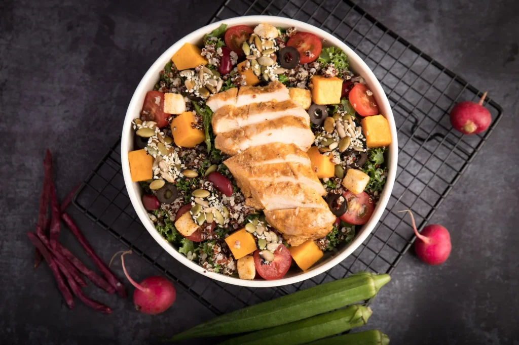 high protein lunch bowls for weight loss with grilled chicken, quinoa, avocado, and cherry tomatoes in a white bowl