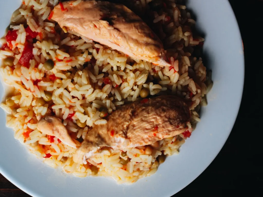instant pot chicken and rice recipe easy with browned chicken thighs, separate white rice grains, and green peas in a stainless pot