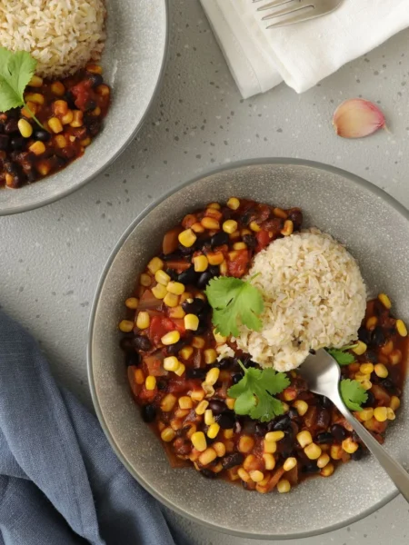 instant pot vegan chili in a white bowl with black beans, kidney beans, brown lentils, and red bell pepper in thick tomato broth