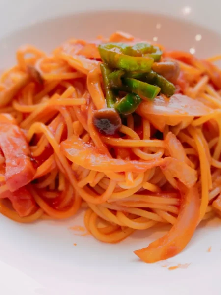 jollof spaghetti recipe with red pepper tomato sauce, spaghetti noodles, and mixed vegetables in a deep pan