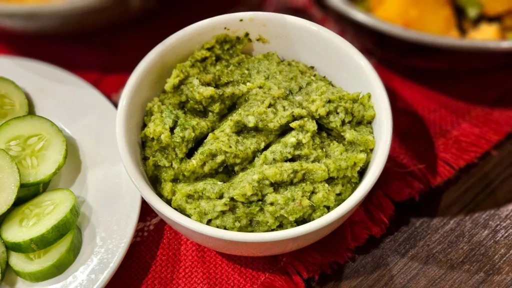 kale pesto recipe in a white bowl showing dark green kale and basil sauce with almond bits and parmesan on a wooden board