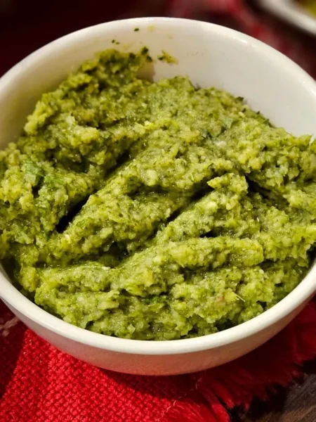 kale pesto recipe in a white bowl showing dark green kale and basil sauce with almond bits and parmesan on a wooden board