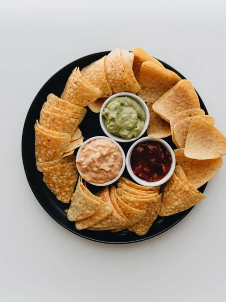 layered bean dip recipe with refried beans, sour cream, guacamole, cheese, and fresh tomato in a glass dish