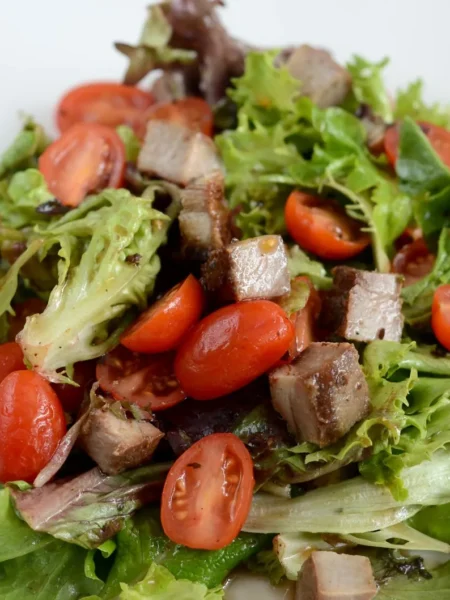 light balsamic vinaigrette in a glass jar poured over mixed greens with tomato slices and cucumber