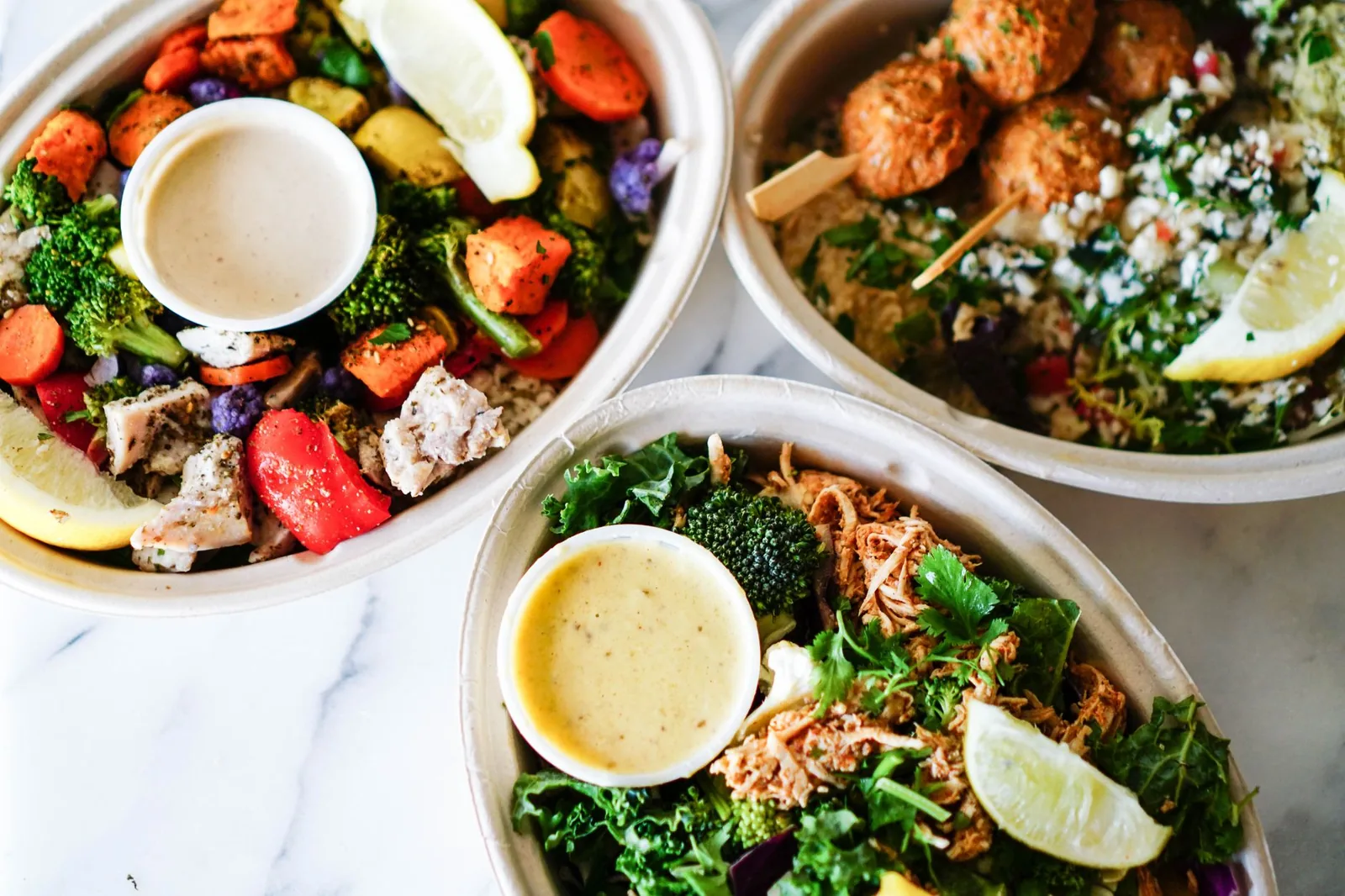 meal prep grain bowls for the week with brown rice, roasted chicken, broccoli, and tahini sauce in clear containers