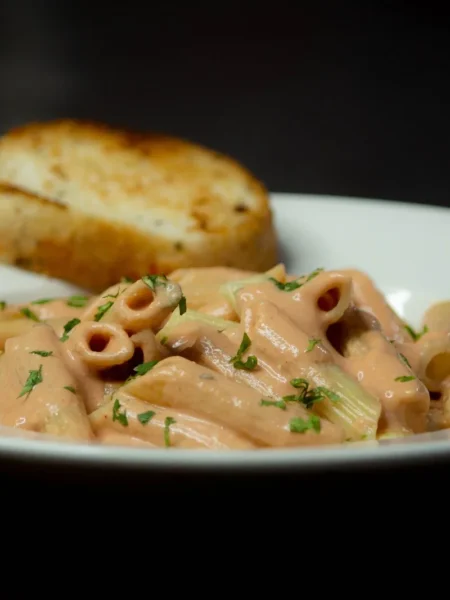 one pot creamy garlic penne pasta with silky parmesan cream sauce, minced garlic, and parsley in a wide pan