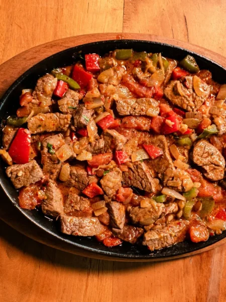 one skillet chicken and vegetables recipe with seared chicken thighs, red and yellow peppers, zucchini, and cherry tomatoes in a cast iron pan