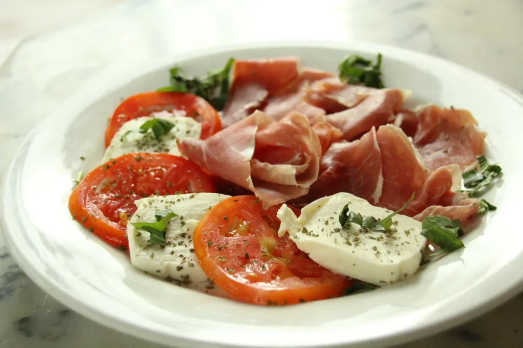 prosciutto wrapped stuffed chicken breasts sliced to show mozzarella and basil filling with crispy cured ham on a white plate