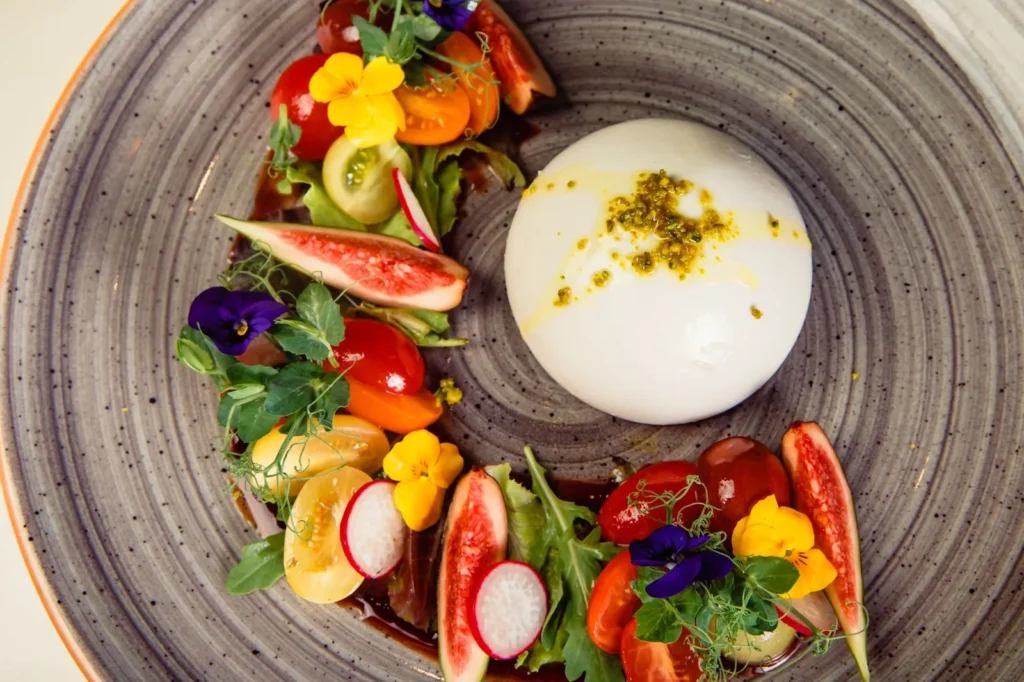 proscuitto burrata and grilled peach salad with grilled peach wedges, creamy burrata, and thin ham on a white plate