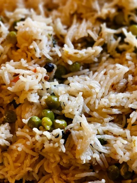 rice veggie pilaf with separate white rice grains, diced carrots, red pepper, and green peas in a shallow bowl