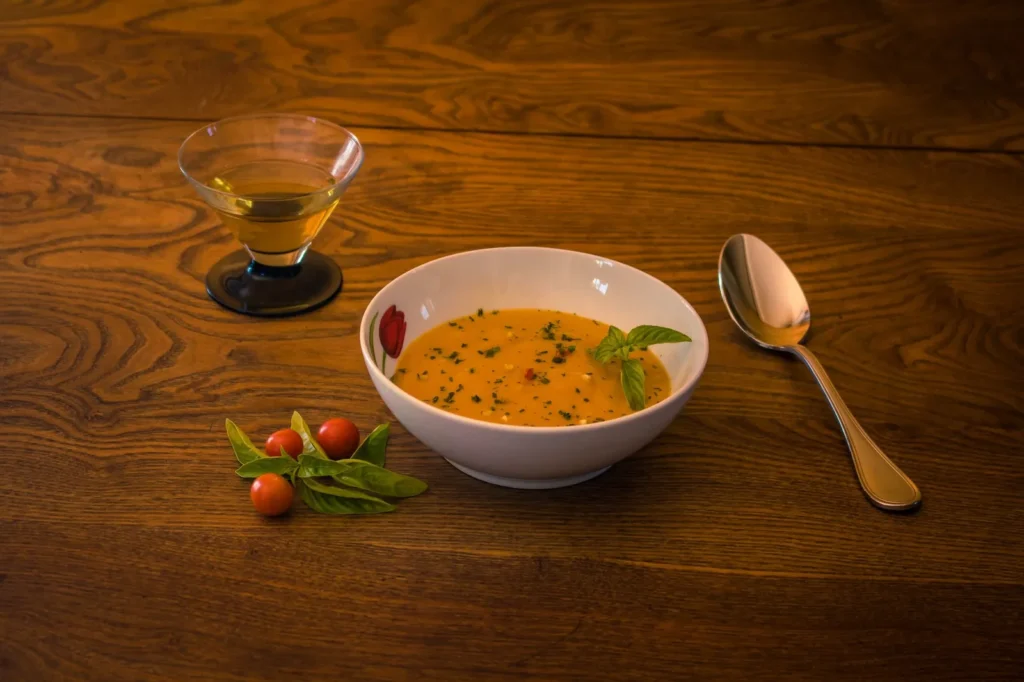 roasted tomato soup recipe in a white bowl with charred tomato pieces, swirled cream, and fresh basil on a wood table