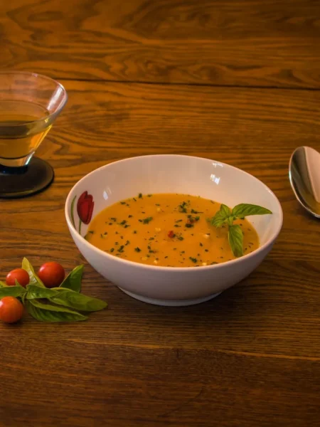 roasted tomato soup recipe in a white bowl with charred tomato pieces, swirled cream, and fresh basil on a wood table