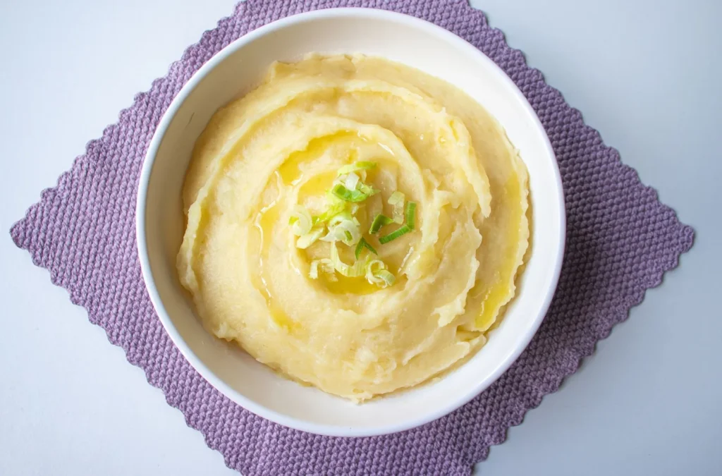 savory mashed sweet potatoes in a white bowl with butter, garlic, and thyme on a rustic table