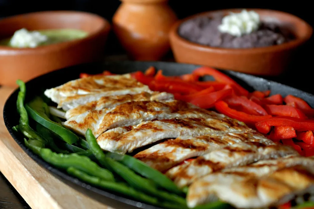 sheet pan chicken fajitas for weeknight dinner with sliced chicken, red and green peppers, and onions on a rimmed tray with tortillas