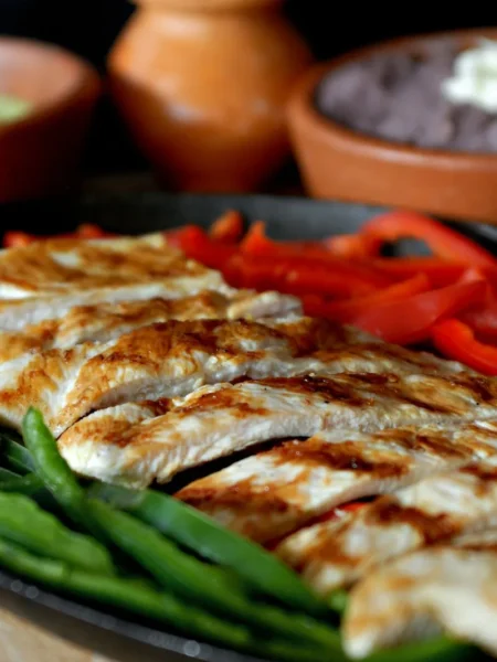 sheet pan chicken fajitas for weeknight dinner with sliced chicken, red and green peppers, and onions on a rimmed tray with tortillas