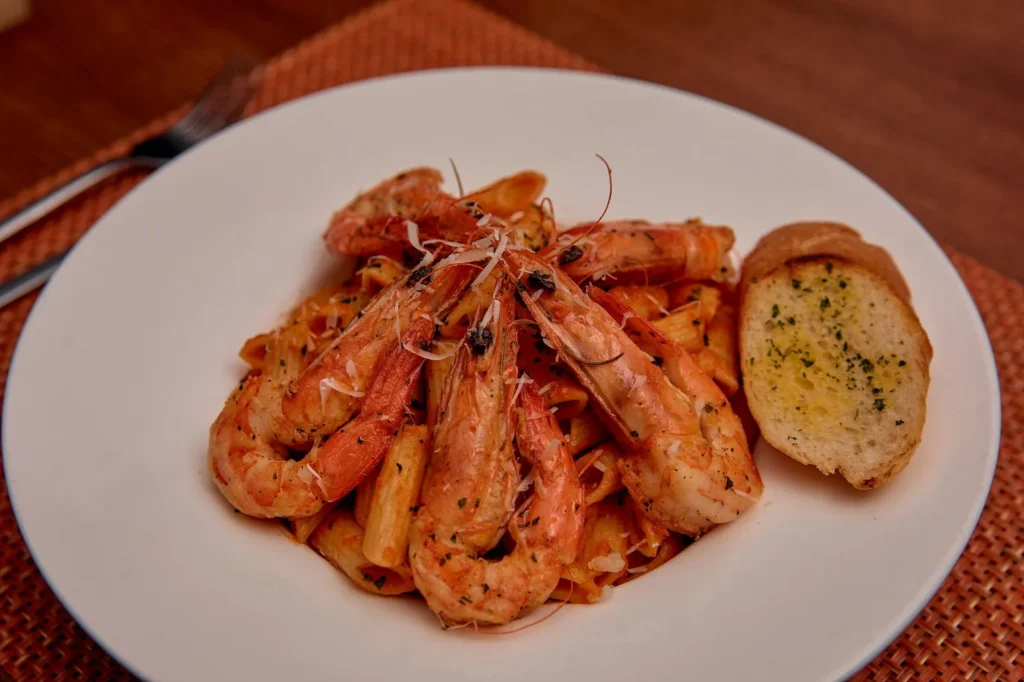 shrimp with vodka sauce served over penne with creamy tomato cream sauce, parsley, and parmesan on a white plate