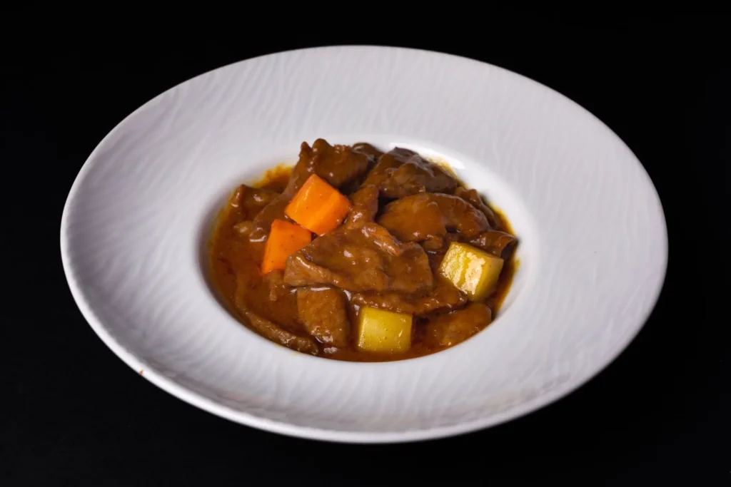 slow cooker irish stew with tender beef chunks, waxy potatoes, and carrots in a dark thick broth in a white bowl