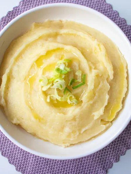 slow cooker mashed potatoes in a white bowl with butter pat and chives on top