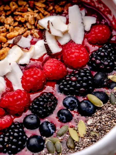 smoothie bowl recipe with frozen berries topped with granola, sliced almonds, and fresh berries in a shallow white bowl