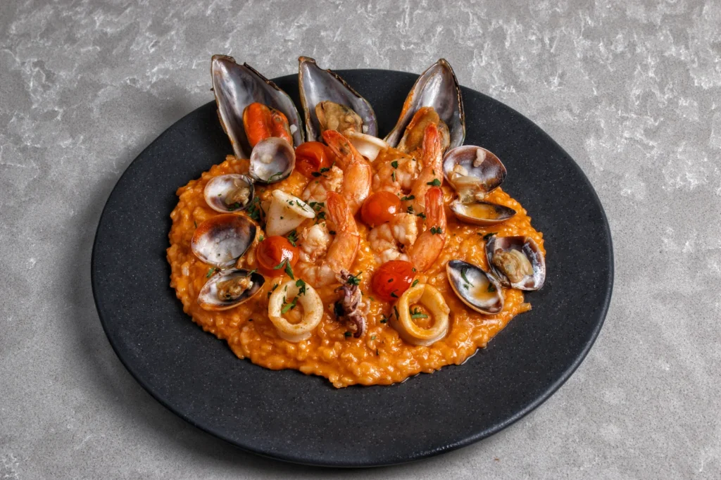 spanish style seafood risotto in a wide pan with pink prawns, open mussels, squid rings, and saffron rice