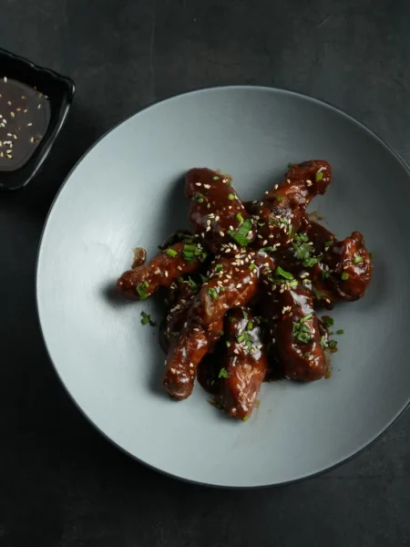 sweet and spicy sesame wings with golden crisp skin, sticky honey sesame glaze, toasted seeds, and sliced green onions on a white plate