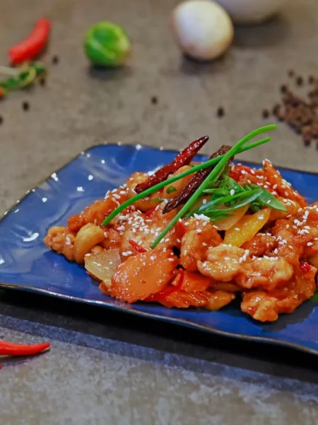 sweet chili chicken stir fry with glossy chicken pieces, red and yellow peppers, and sesame seeds in a wok
