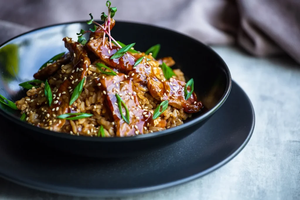 teriyaki ground beef bowls with glossy beef crumbles, white rice, shredded cabbage, carrots, and sesame seeds in a shallow bowl